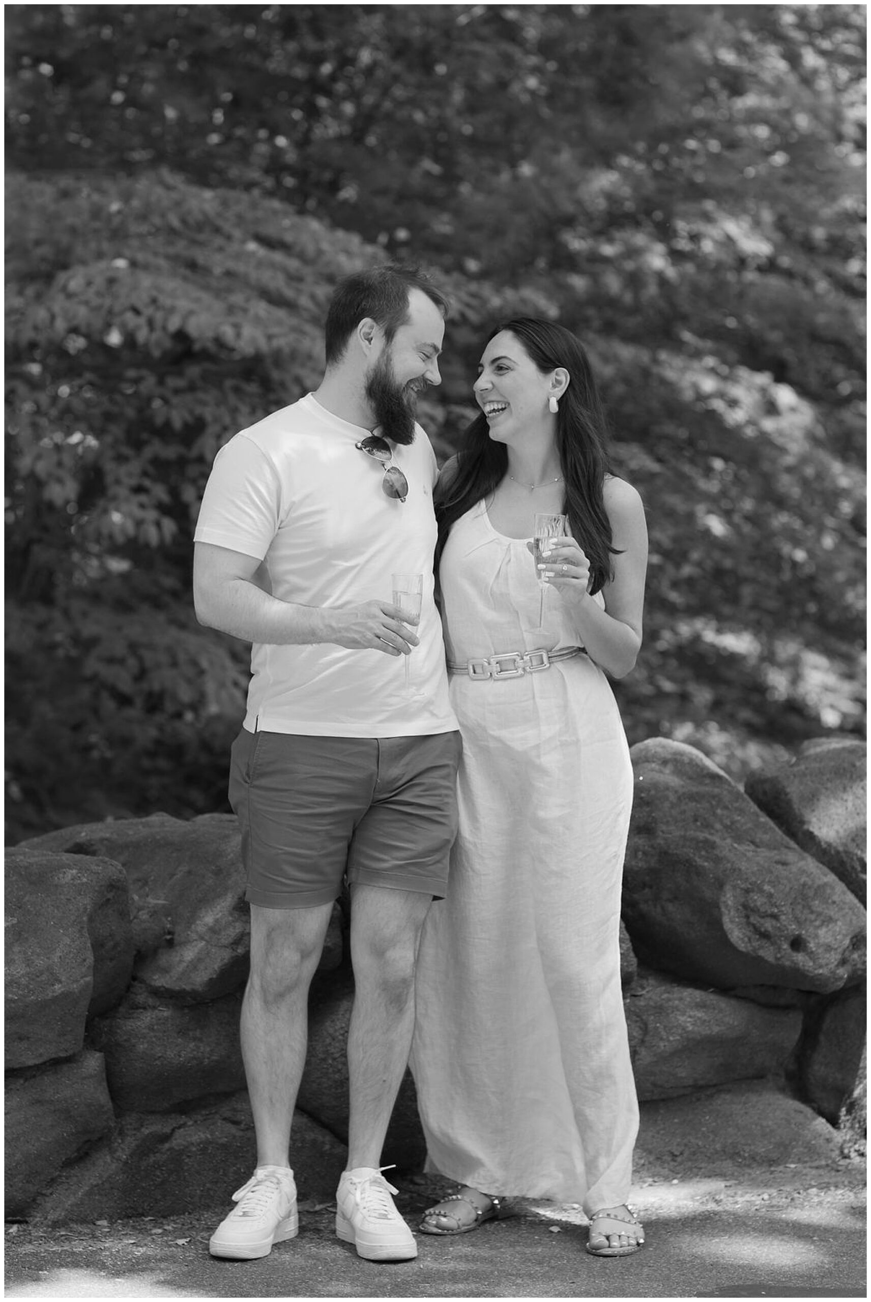A newly engaged couple stands by some rocks in a park drinking champagne dc engagement photographer
