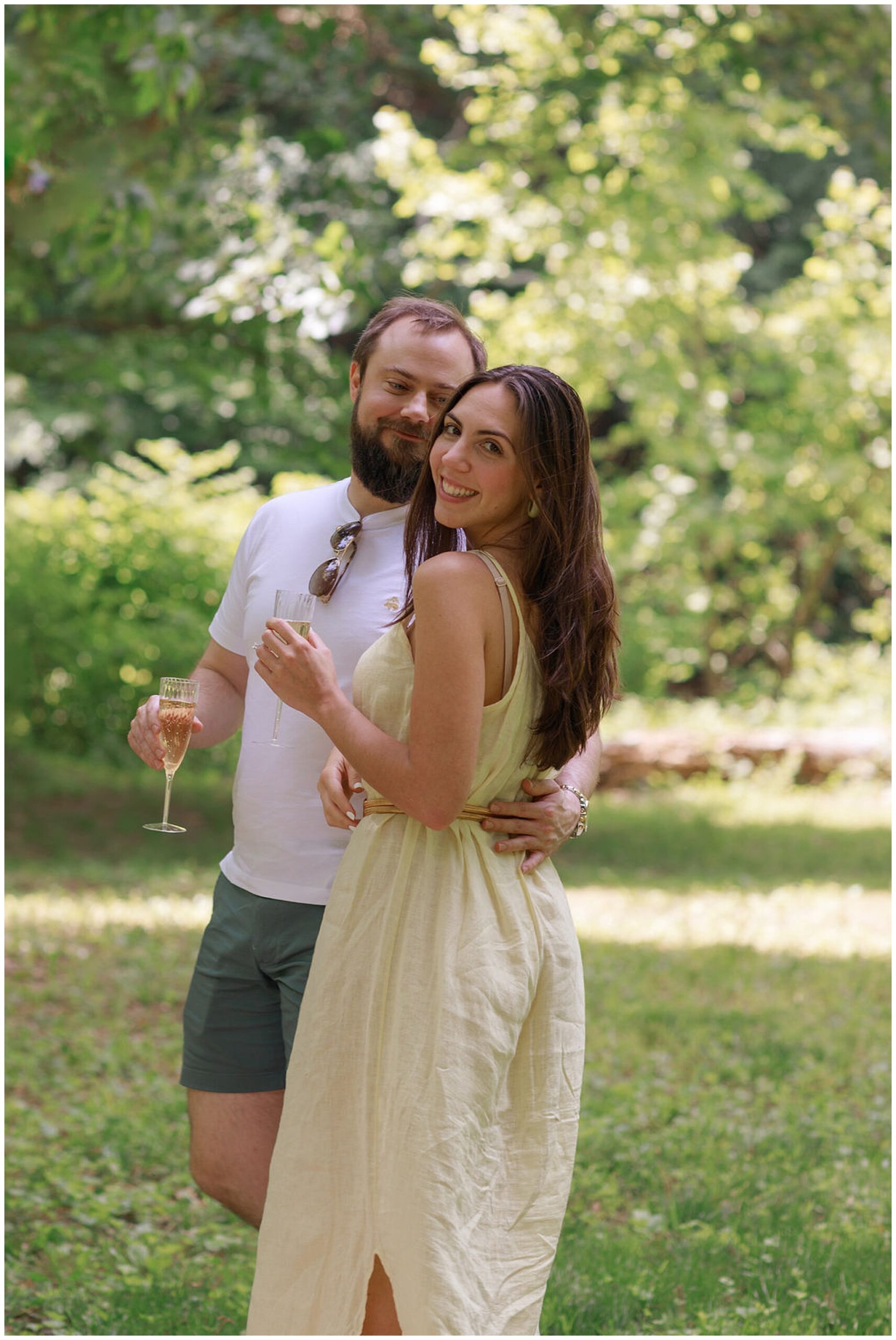 A man gazes at his fiance while drinking champagne in a park dc engagement photographer