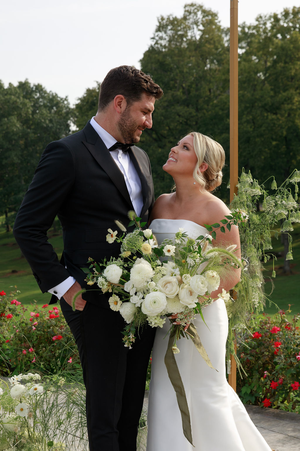 Newlyweds gaze at each other while standing in a rose garden and holding a large white bouquet washington dc wedding florist