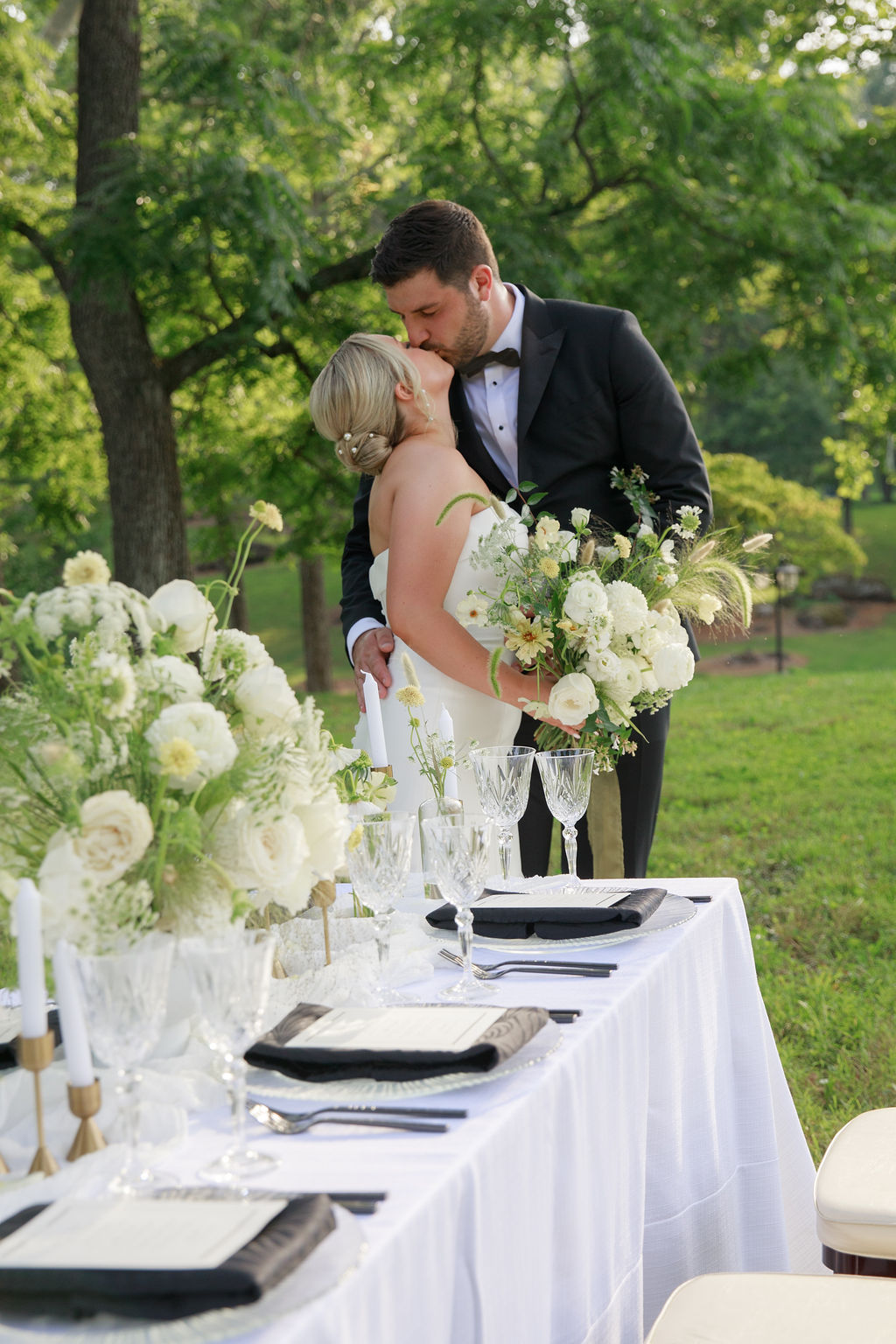Newlyweds kiss next to their small outdoor reception table with white flower bouquets washington dc wedding florist