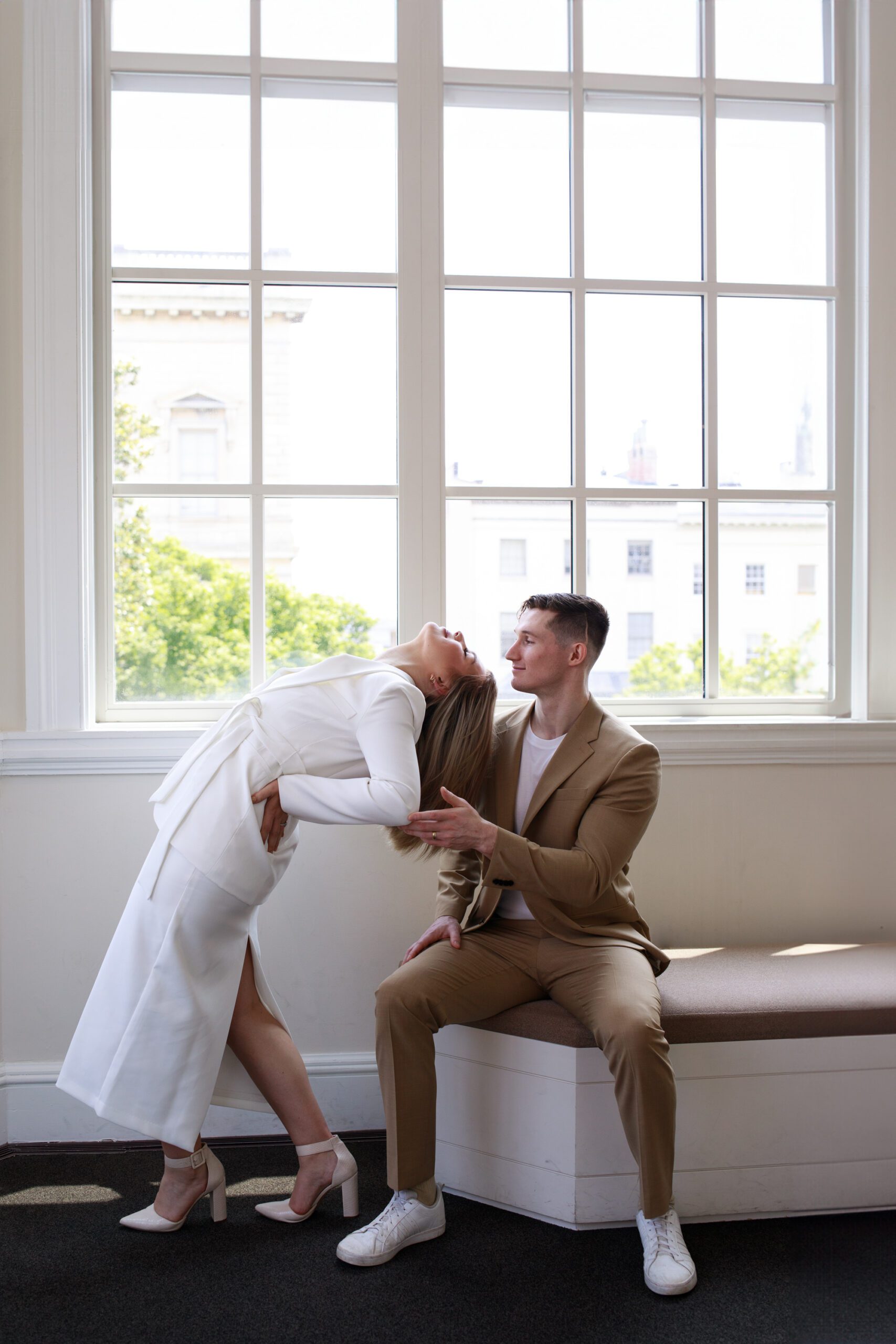 Unique art gallery engagement photos. The bride is arching her back in a romantic way towards her groom, who is seated nearby.
