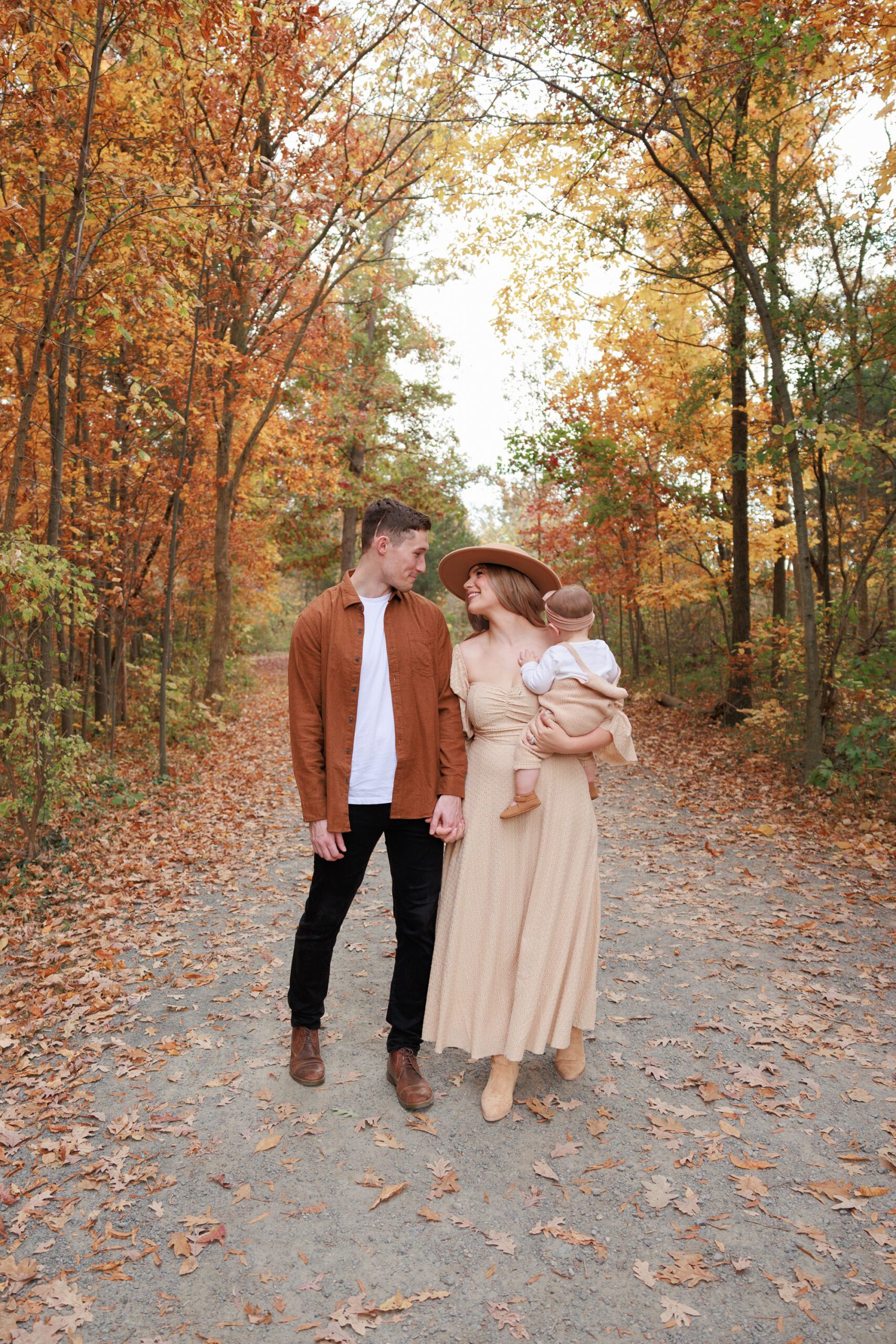 Mom, dad, and baby looking cute together in their neutral outfits that blend in with the autumn foliage.