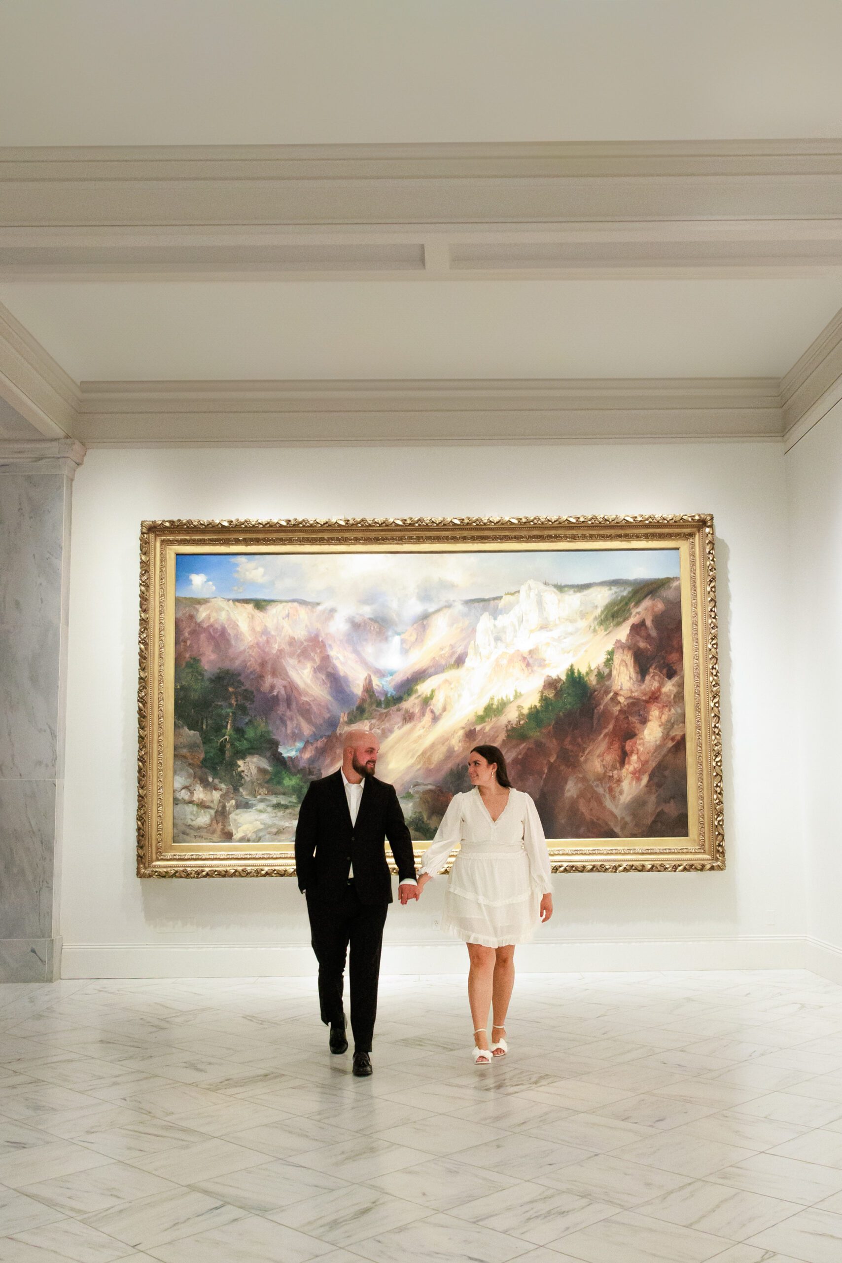 A couple embraces for their engagement photos at the National Portrait Gallery in Washington DC. They are holding hands in front of a large piece of art.