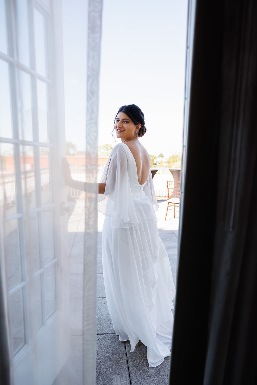 A bride holds the door open while walking out onto her balcony at the lorien hotel wedding venue