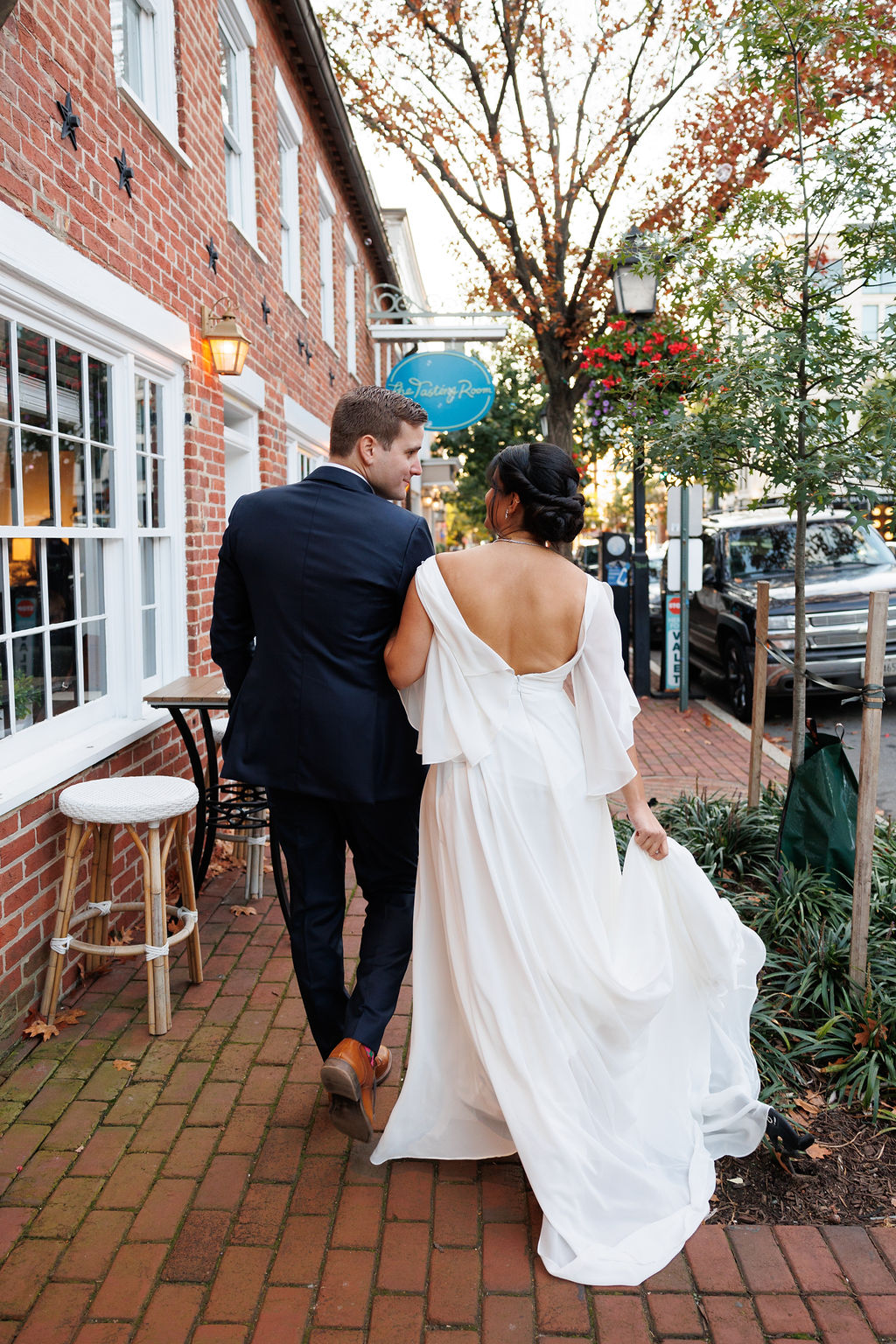 Newlyweds hold hands while walking on the brick sidewalk and holding the train