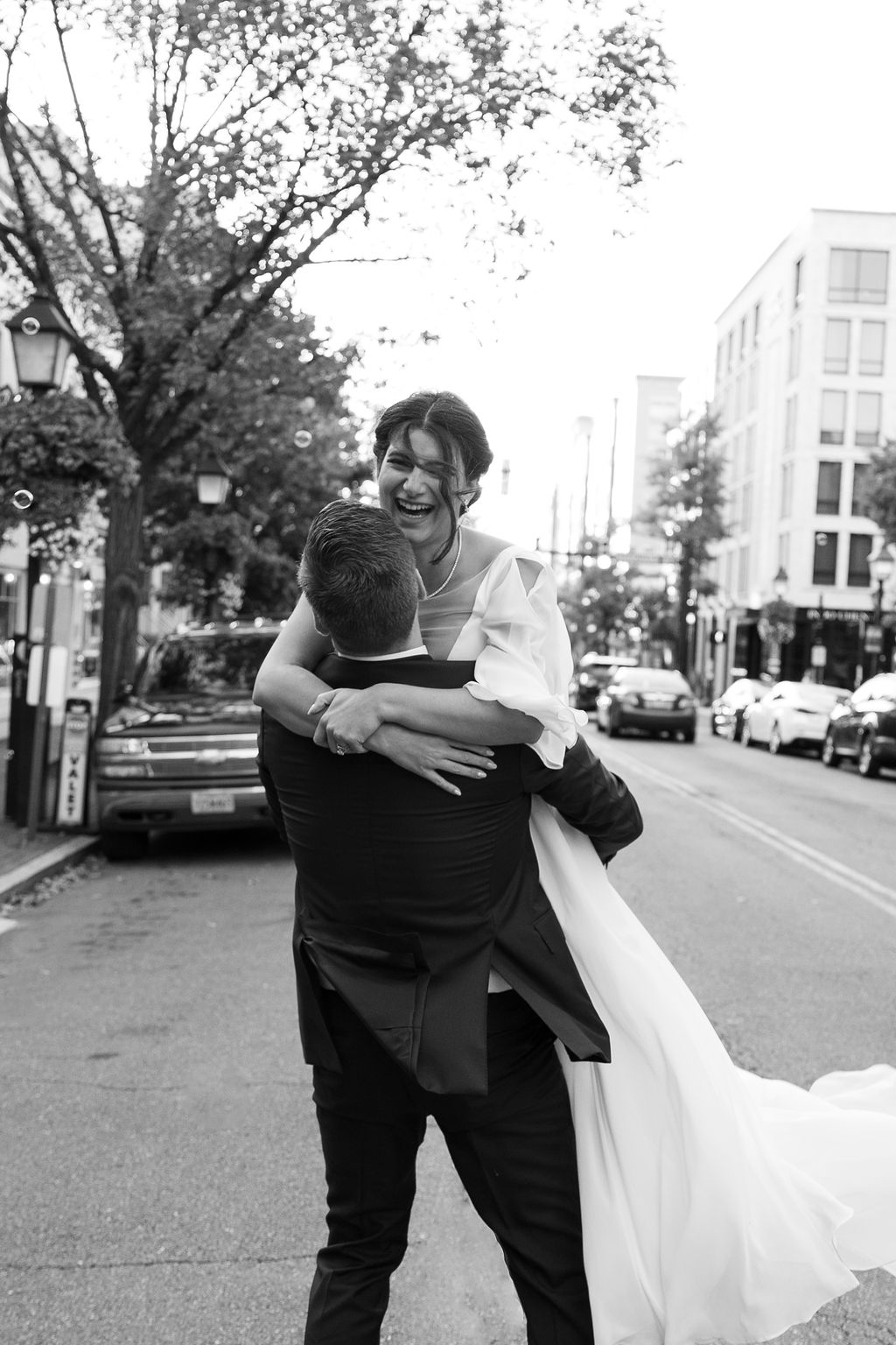 Newlyweds laugh and celebrate as the groom lifts his bride in the street