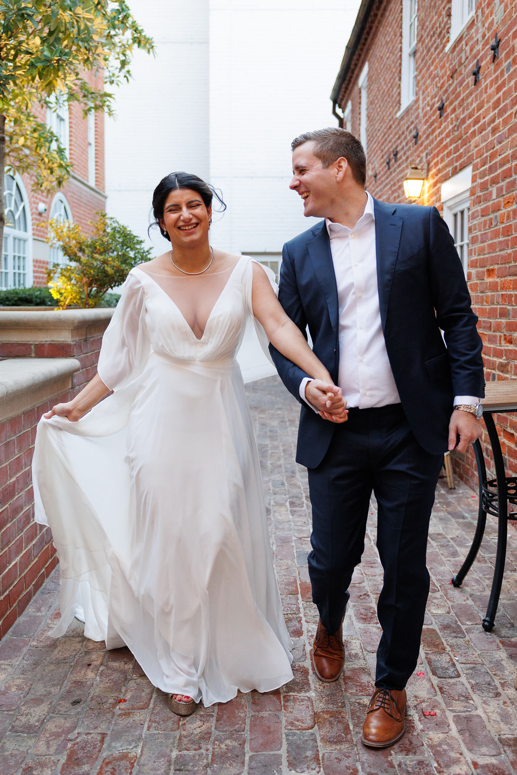 Newlyweds laugh and hold hands while walking in an alley