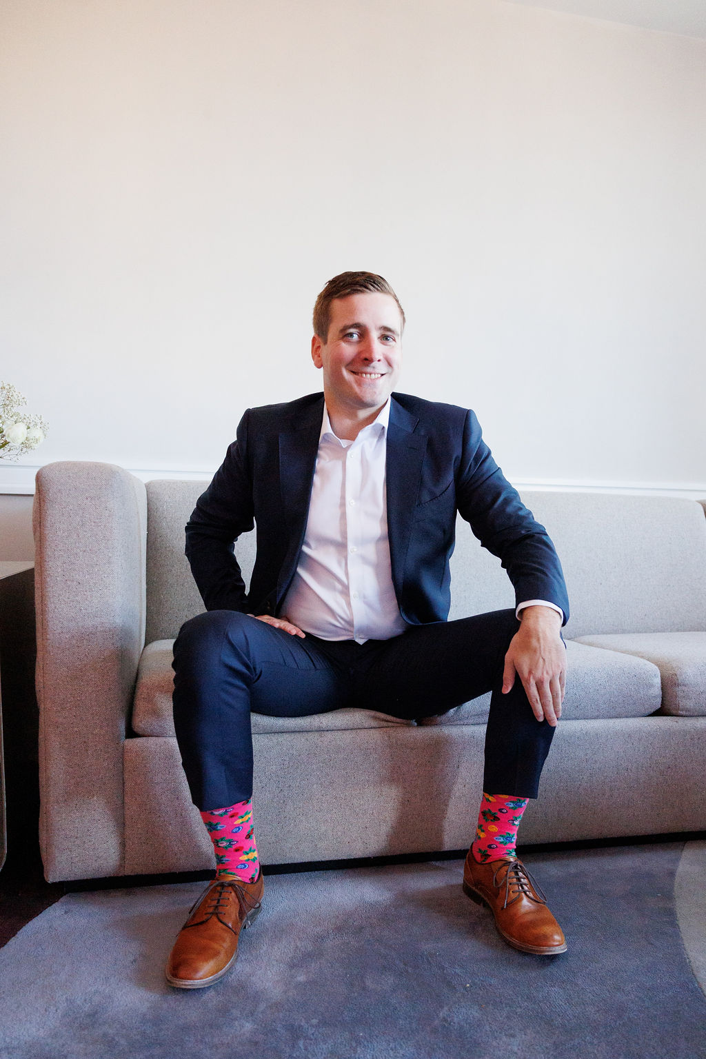 A groom shows off his fun pink socks while sitting on a couch