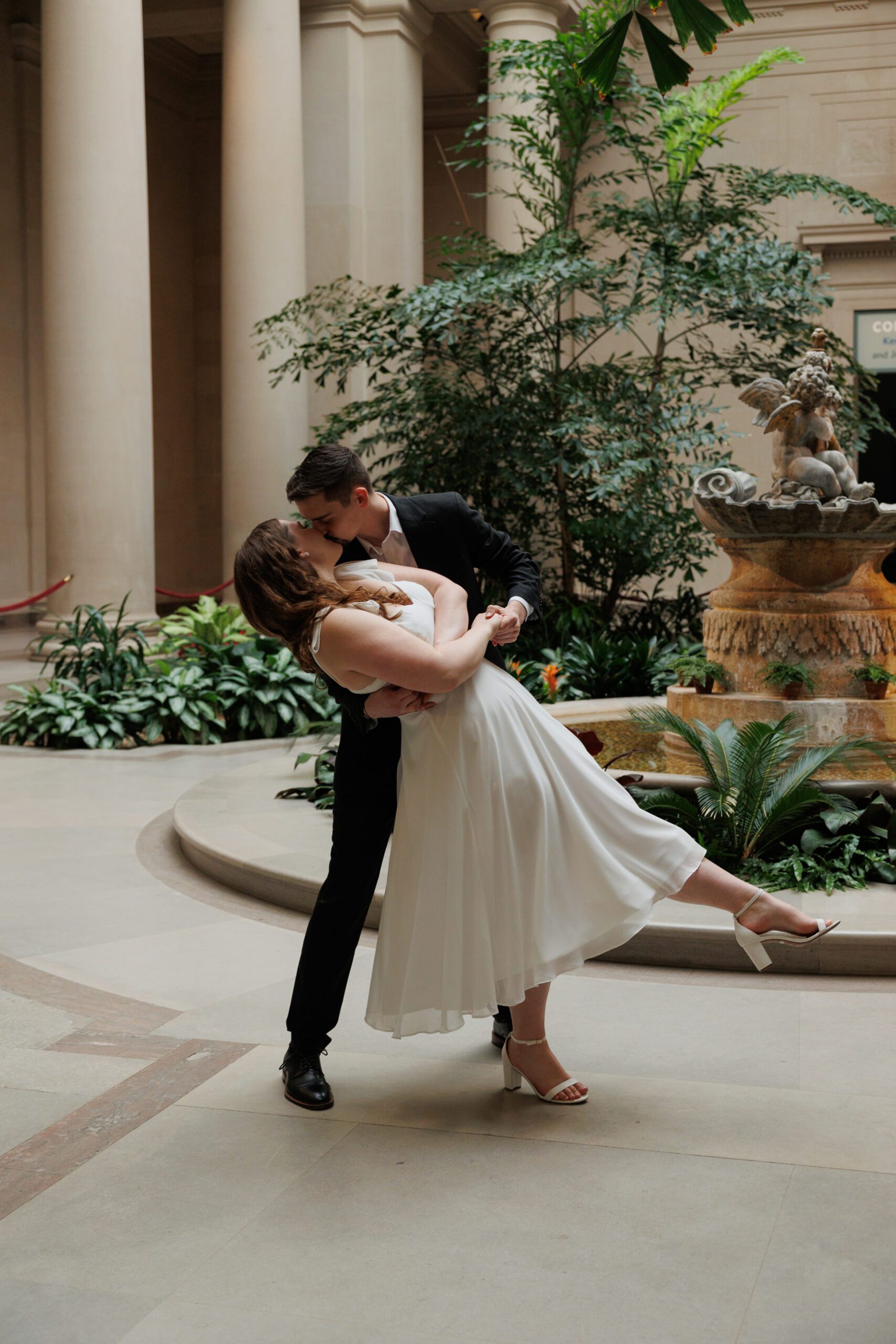 A newly engaged couple dip kiss for their engagement photos in the west building in the national gallery of art