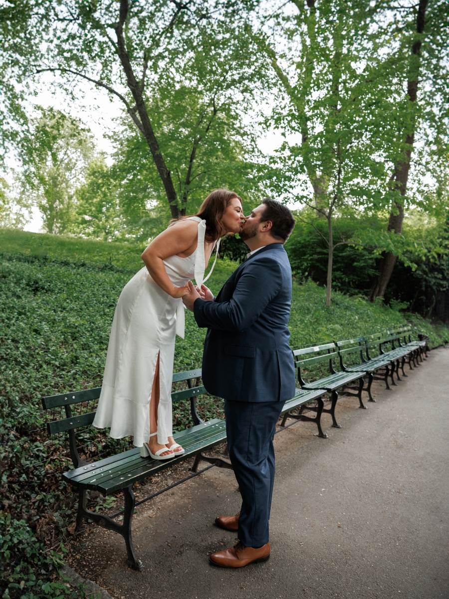 Couple poses for their engagement photos on the park bench in Central Park